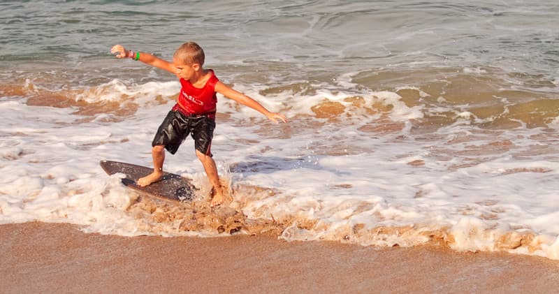 Child skimboarding through shallow shore break at sandy beach
