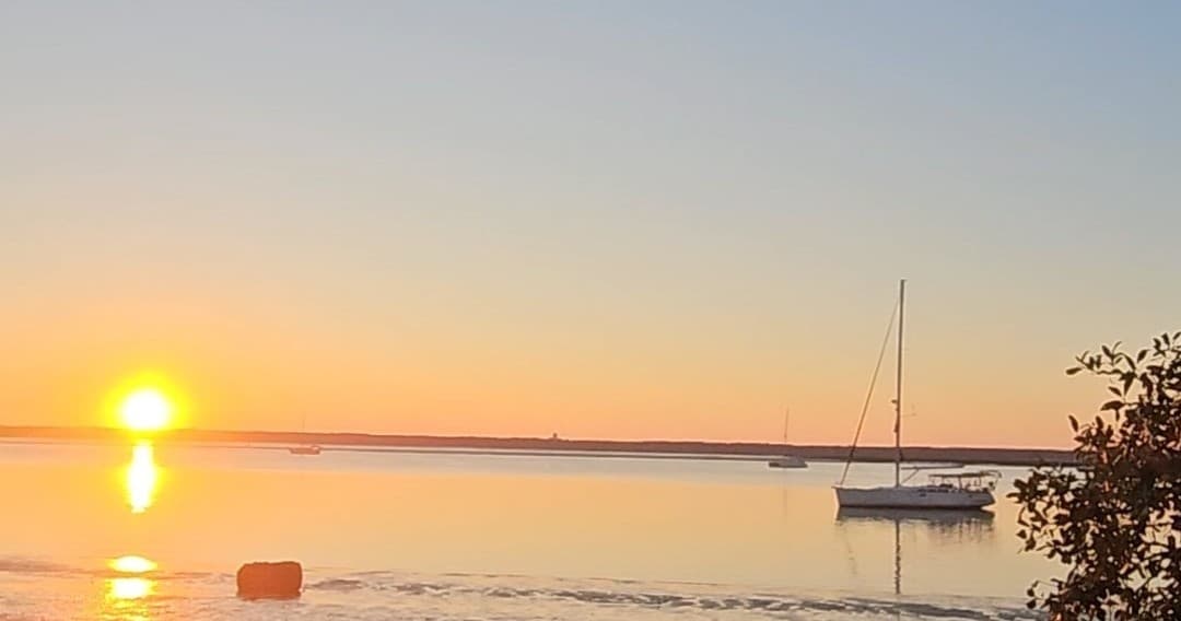 Calm sunrise over bay with moored sailboat and reflections
