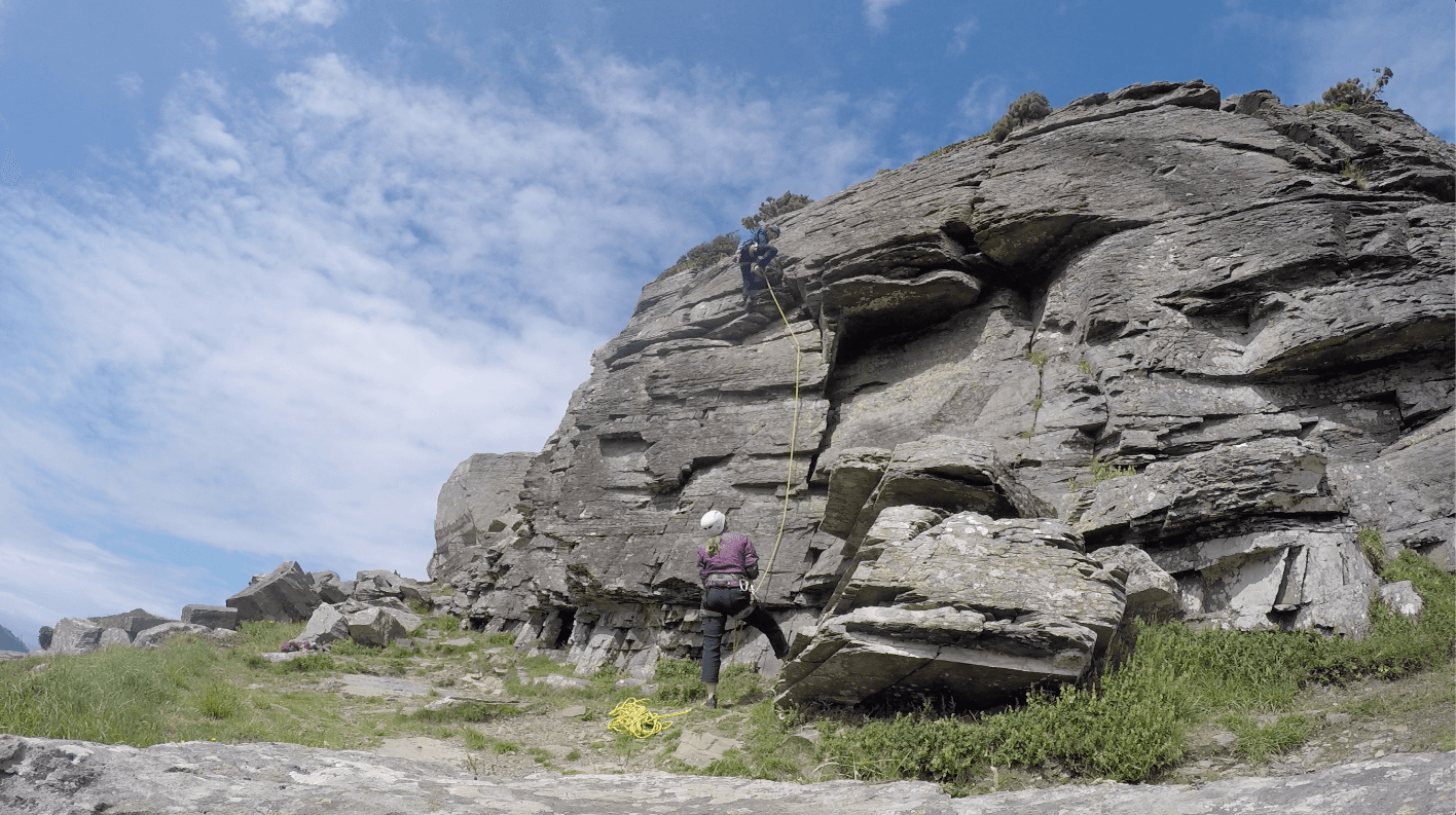 Rock climbers ascending a rugged mountain crag under blue sky