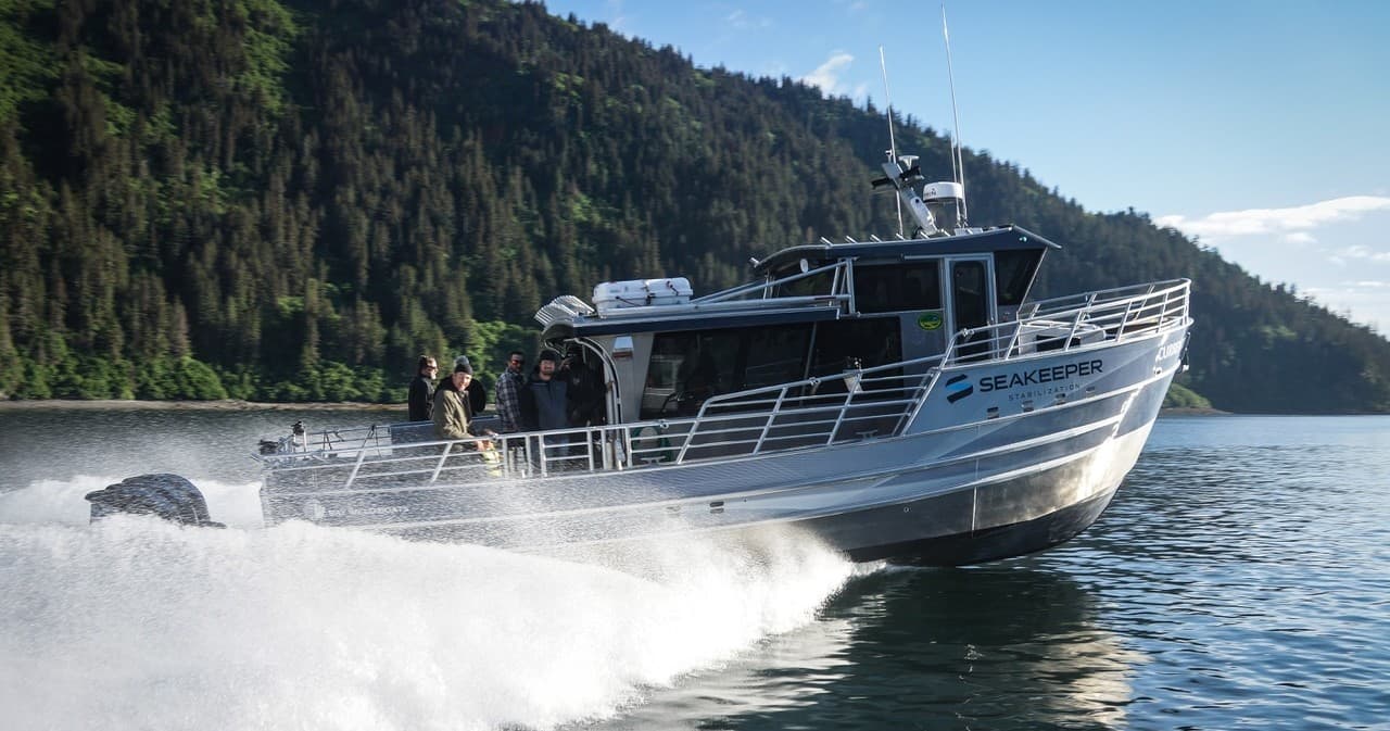 Fishing charter speeding past tree-lined shoreline in calm bay