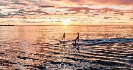 Two standup paddleboarders at sunset on calm ocean near shore