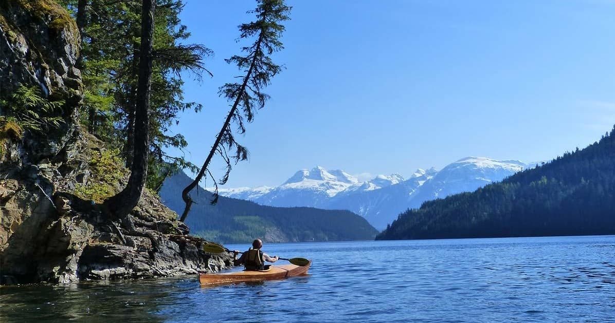 Solo kayaker paddling on alpine lake with snowcapped mountains