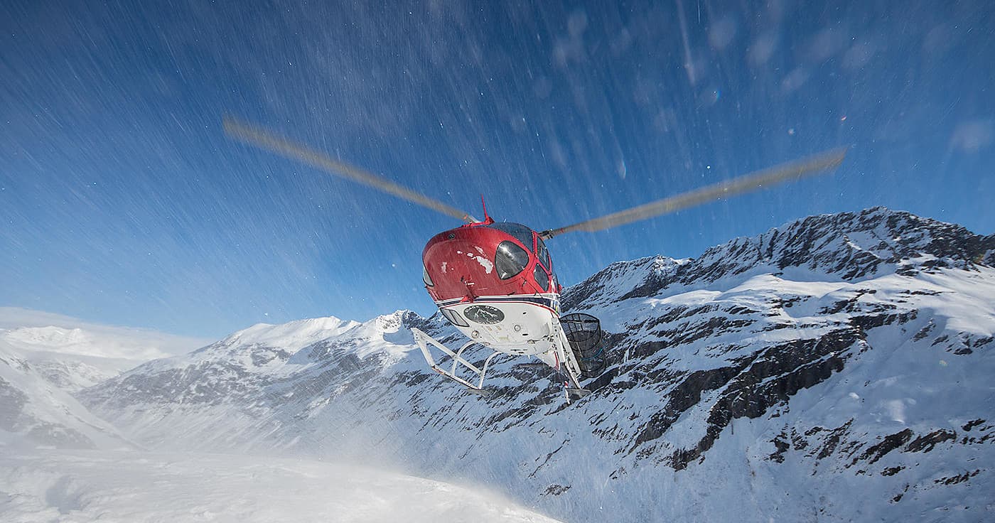 Helicopter dropping skiers over snowy alpine peaks in Alaska