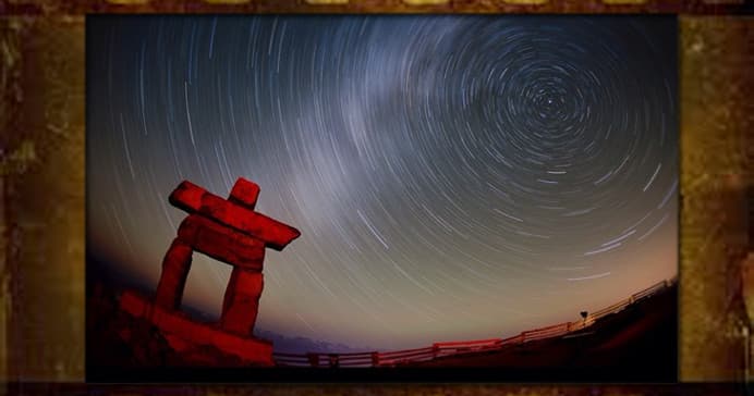 Star trail night sky over stone inuksuk on remote coastal plain