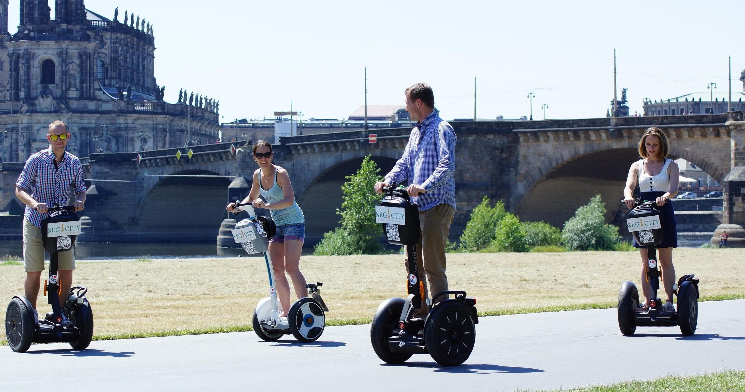 Tourists riding Segways along riverfront with stone bridge