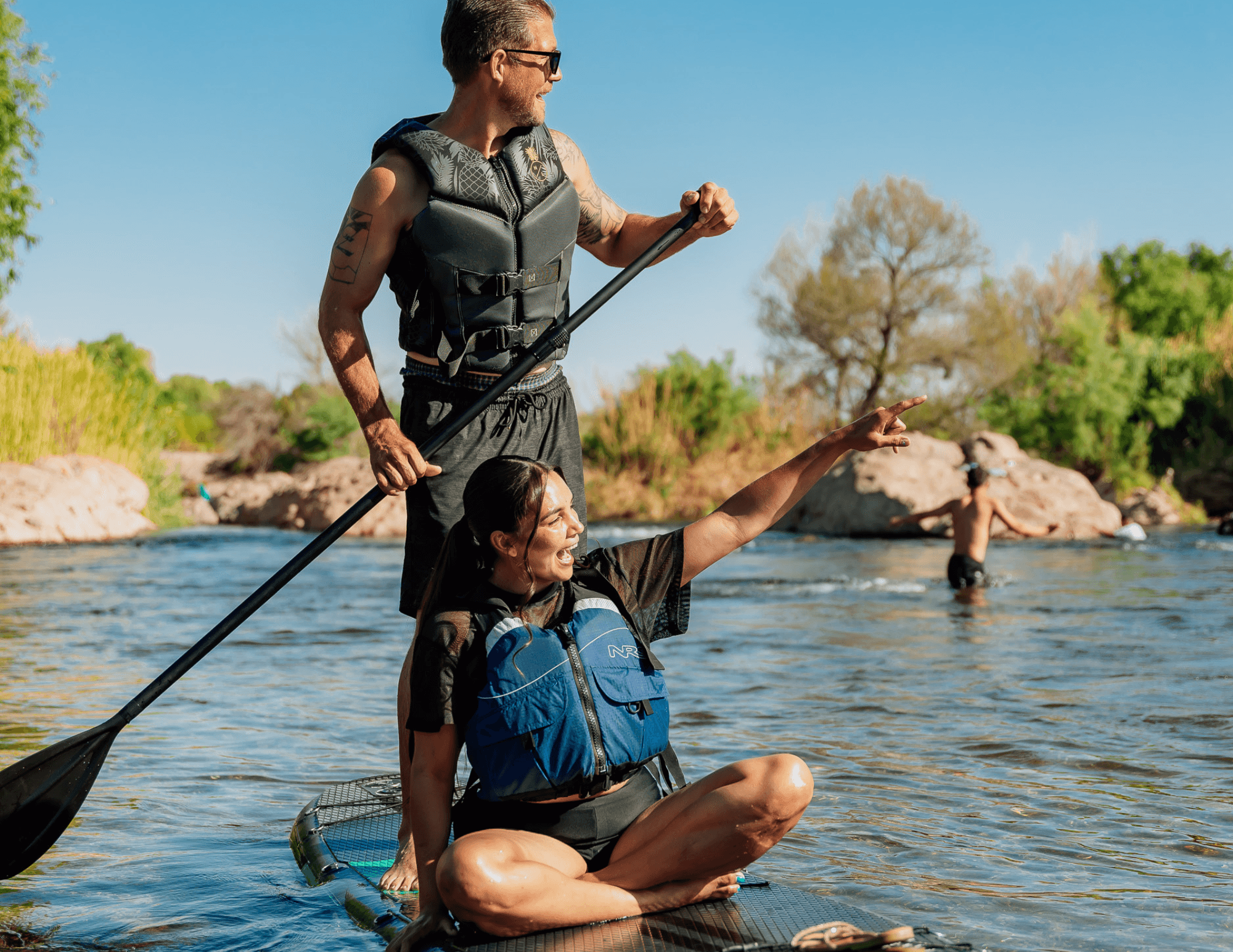 Couple paddling kayaks down a scenic river with desert trees
