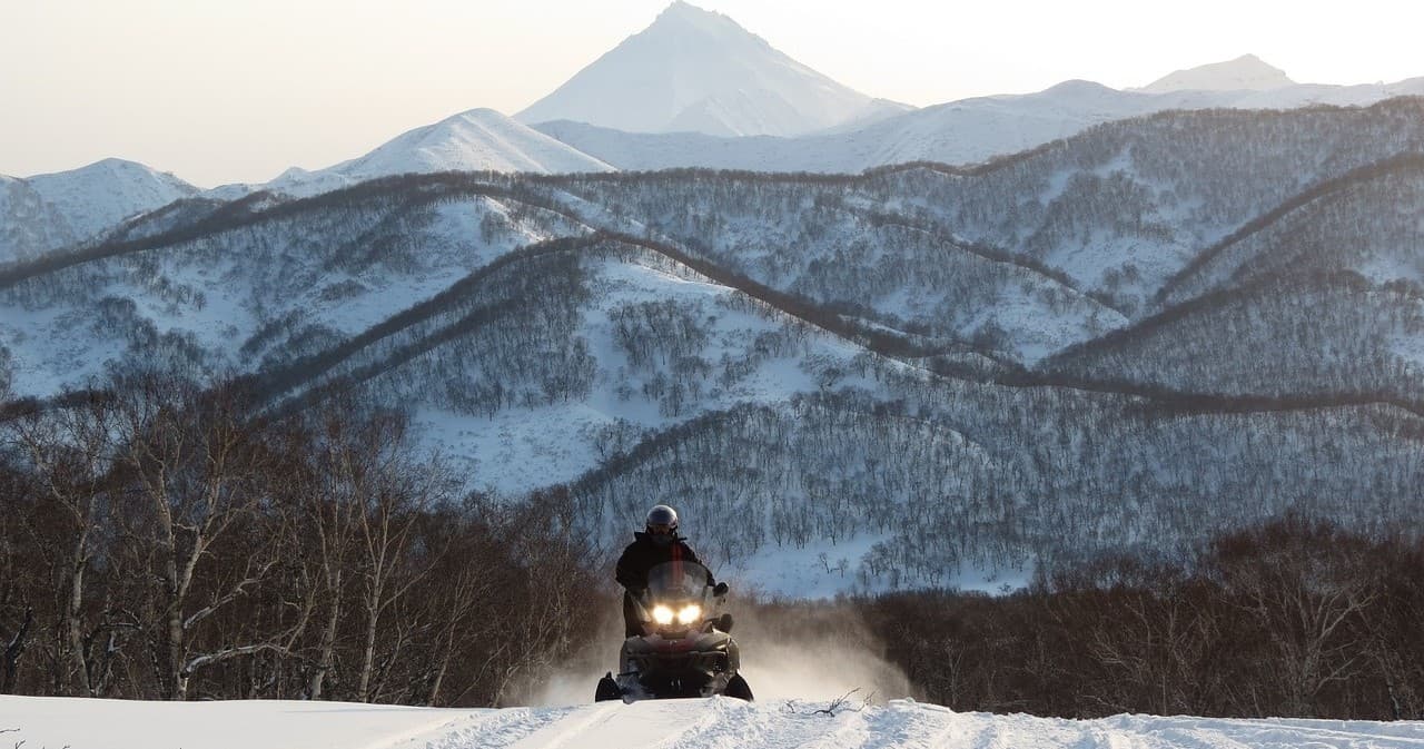 Snowmobiler riding toward mountain ranges in alpine winter wilderness
