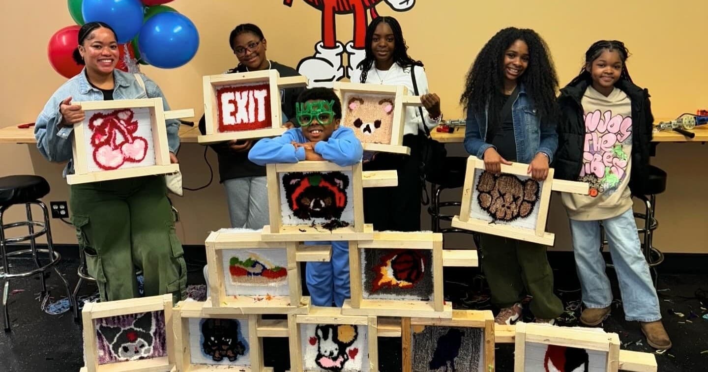 Group posing with tufted rug frames in indoor craft studio