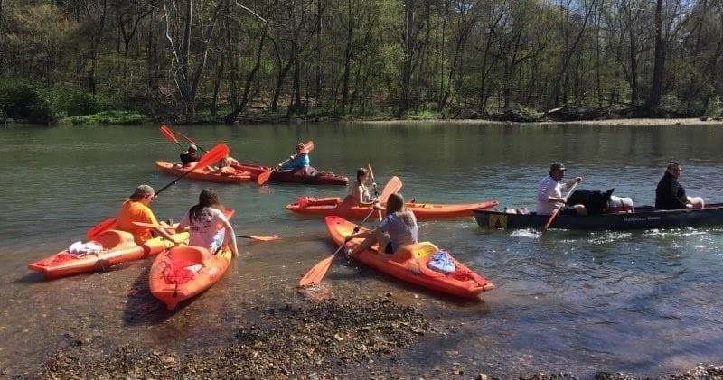 Kayakers paddling on shallow scenic river near wooded shore