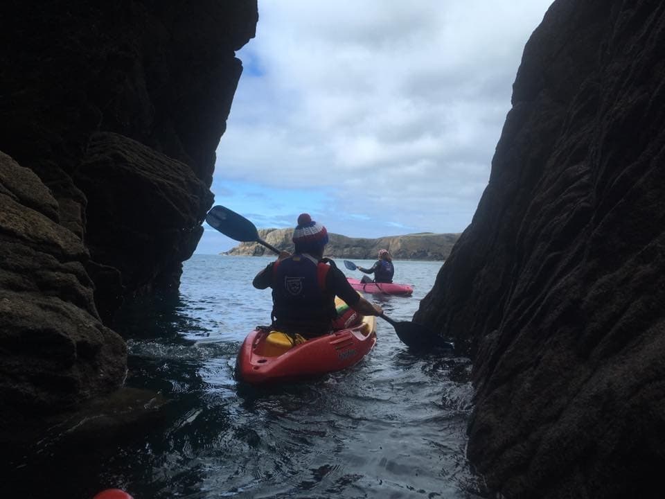 Sea kayaker navigating narrow rocky cave passage at coast