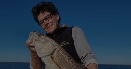 Angler posing with large fish against clear blue ocean sky