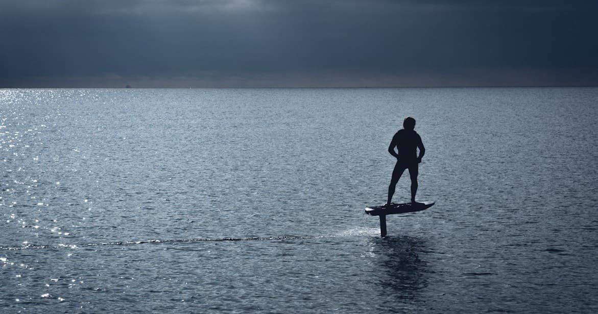 Silhouetted foil surfer on tranquil water with sunlit ripples