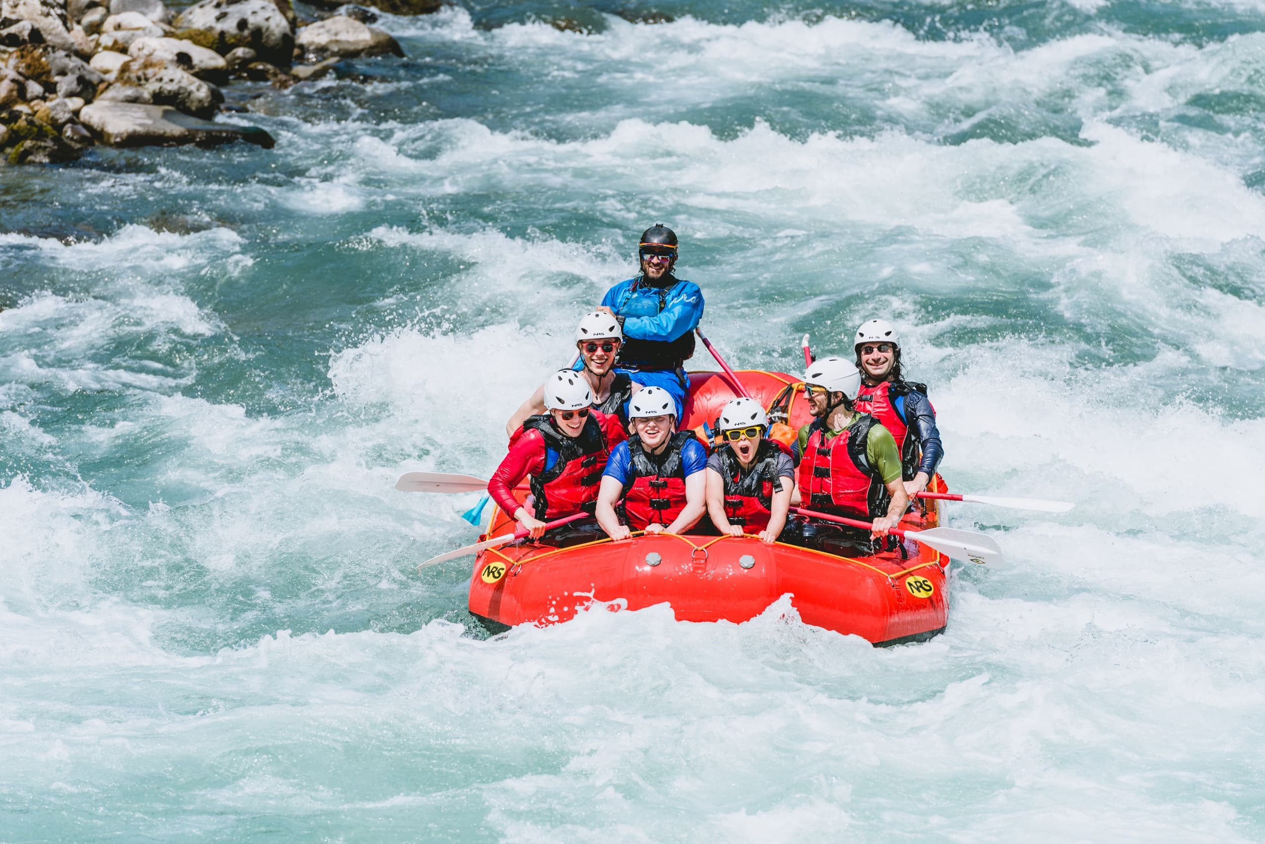 Whitewater raft team riding turbulent turquoise rapids near rocks