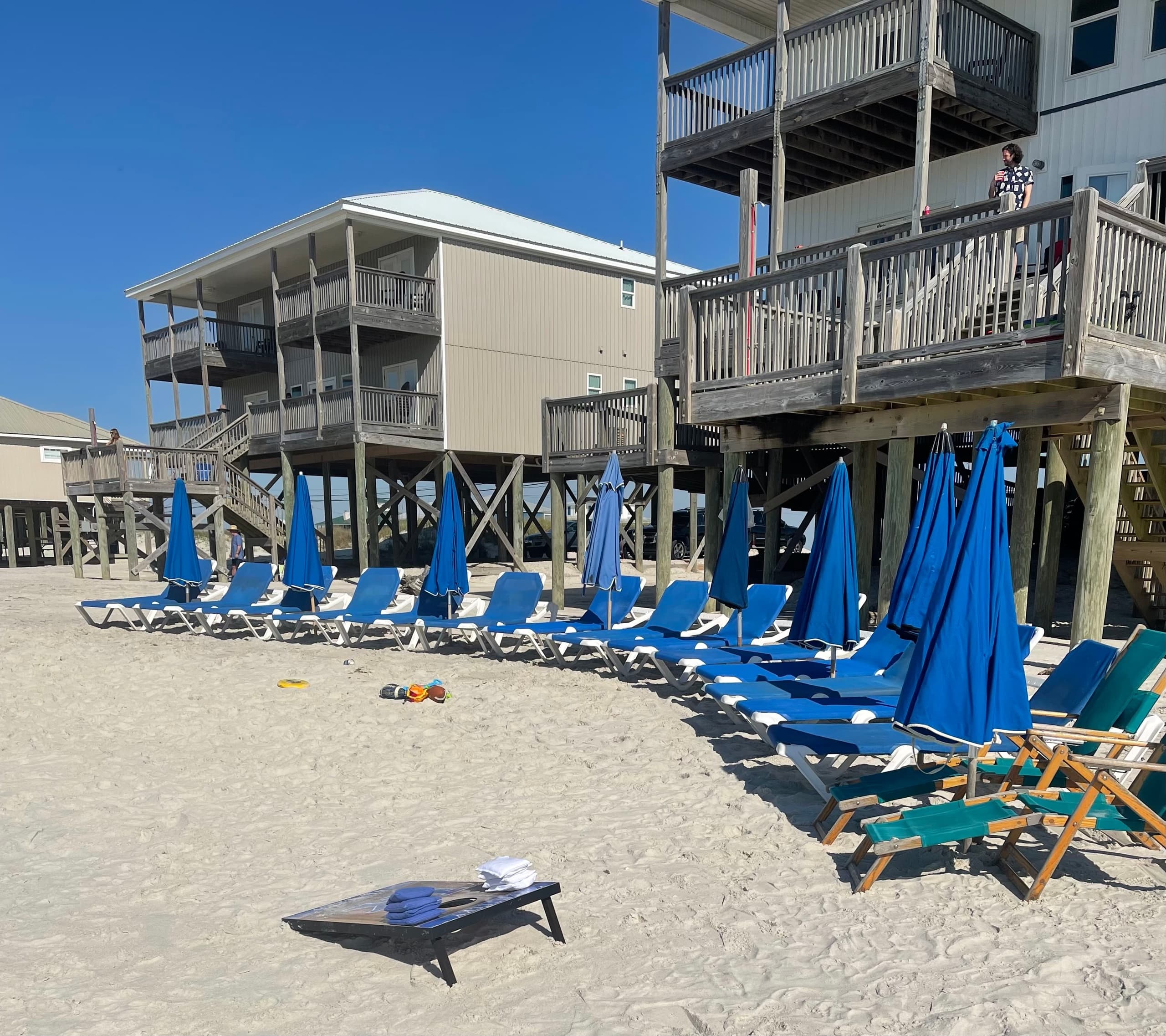 Multiple blue beach loungers and umbrellas near beachfront houses