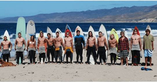Group of surfers posing with boards along shoreline at beach