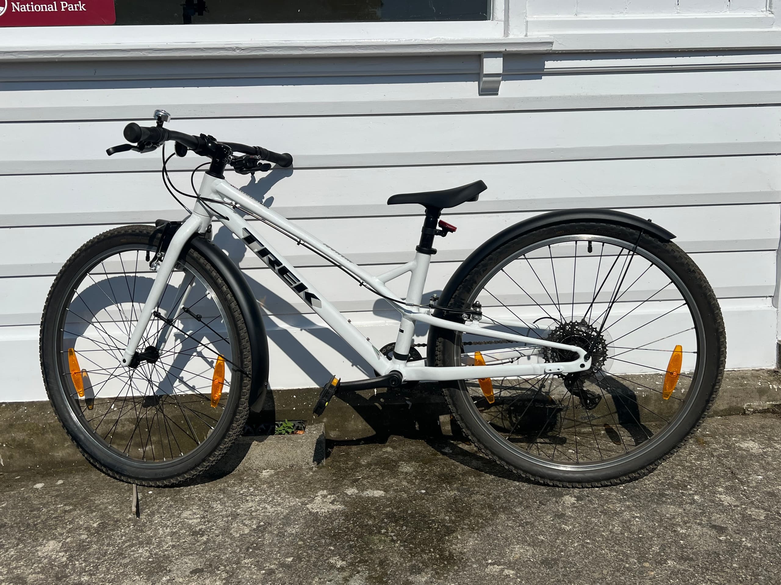 White rental mountain bike parked outdoors on pavement by house siding
