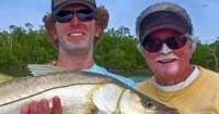 Two anglers smiling holding snook on coastal flats fishing trip