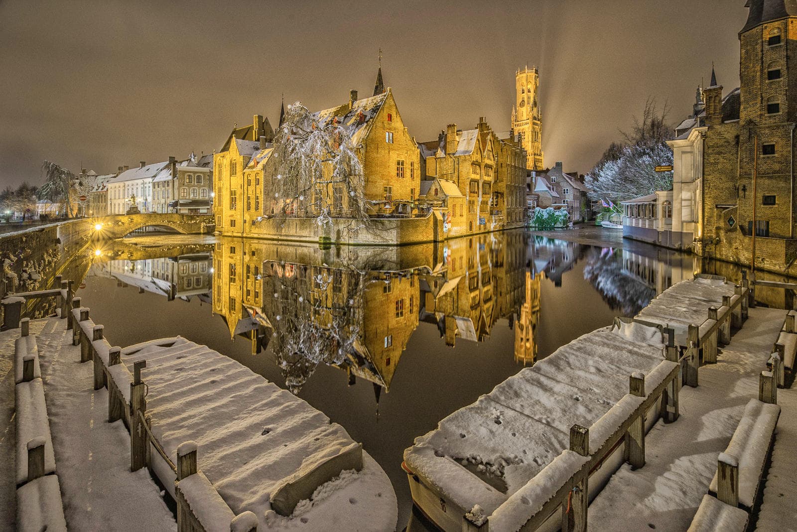 Snowy medieval canal reflecting illuminated Bruges buildings at night