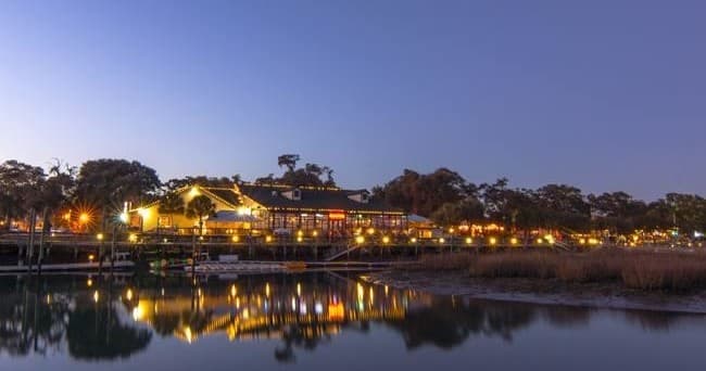 Evening waterfront scene with lit marina reflecting over calm bay