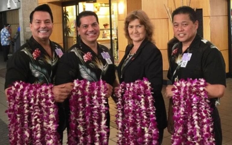 Lei greeting team holding dense purple garlands at arrivals counter
