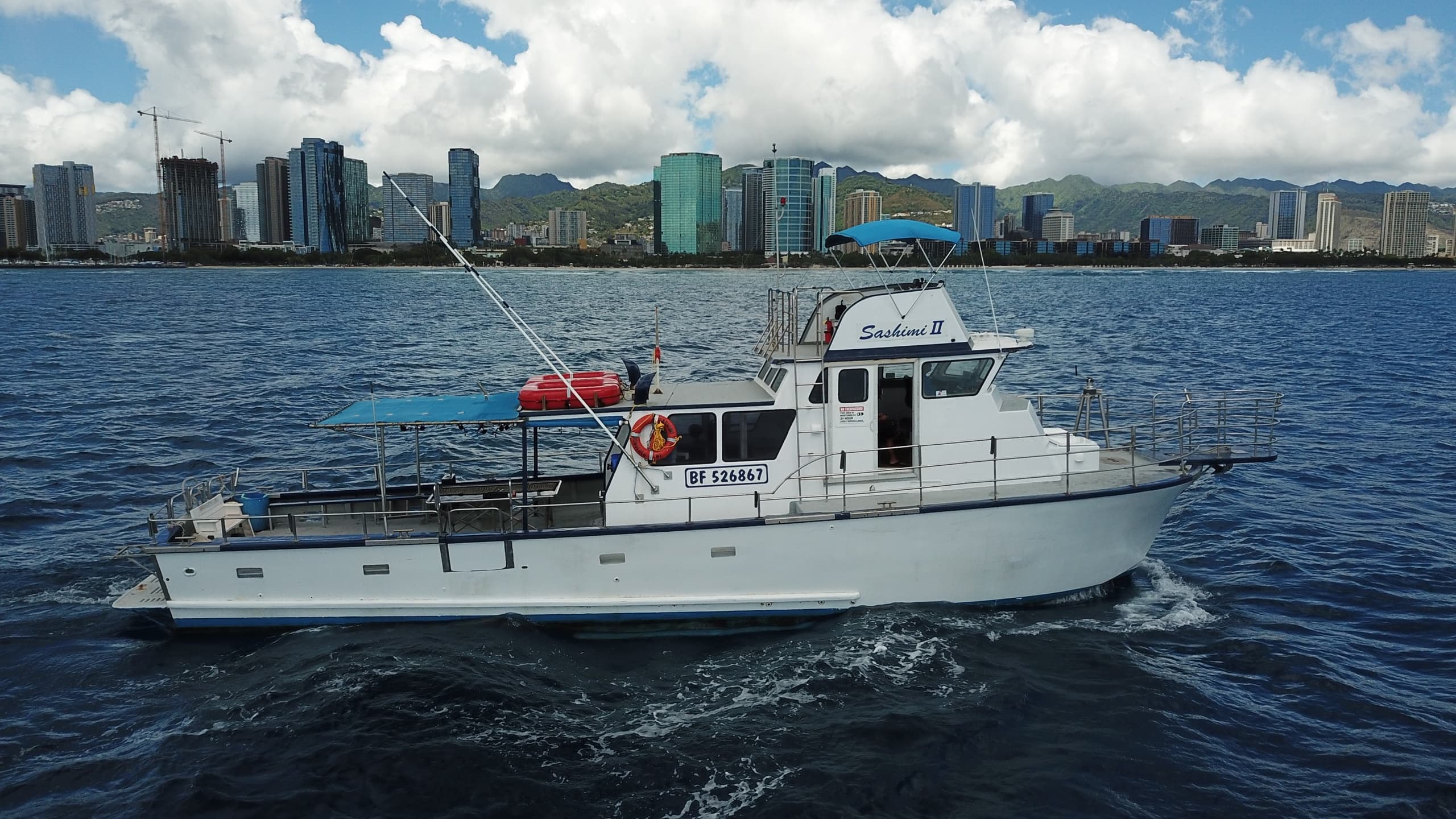 Charter fishing boat cruising past Waikiki skyline under clouds