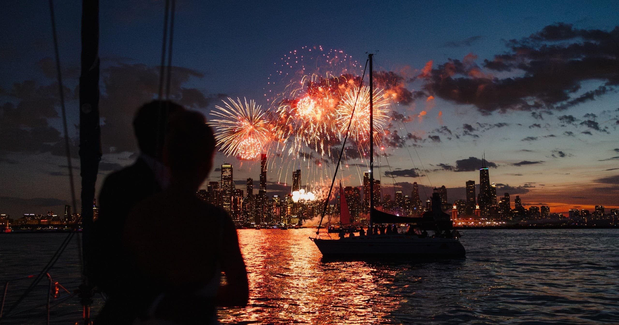 Fireworks over city skyline viewed from sailboat at dusk
