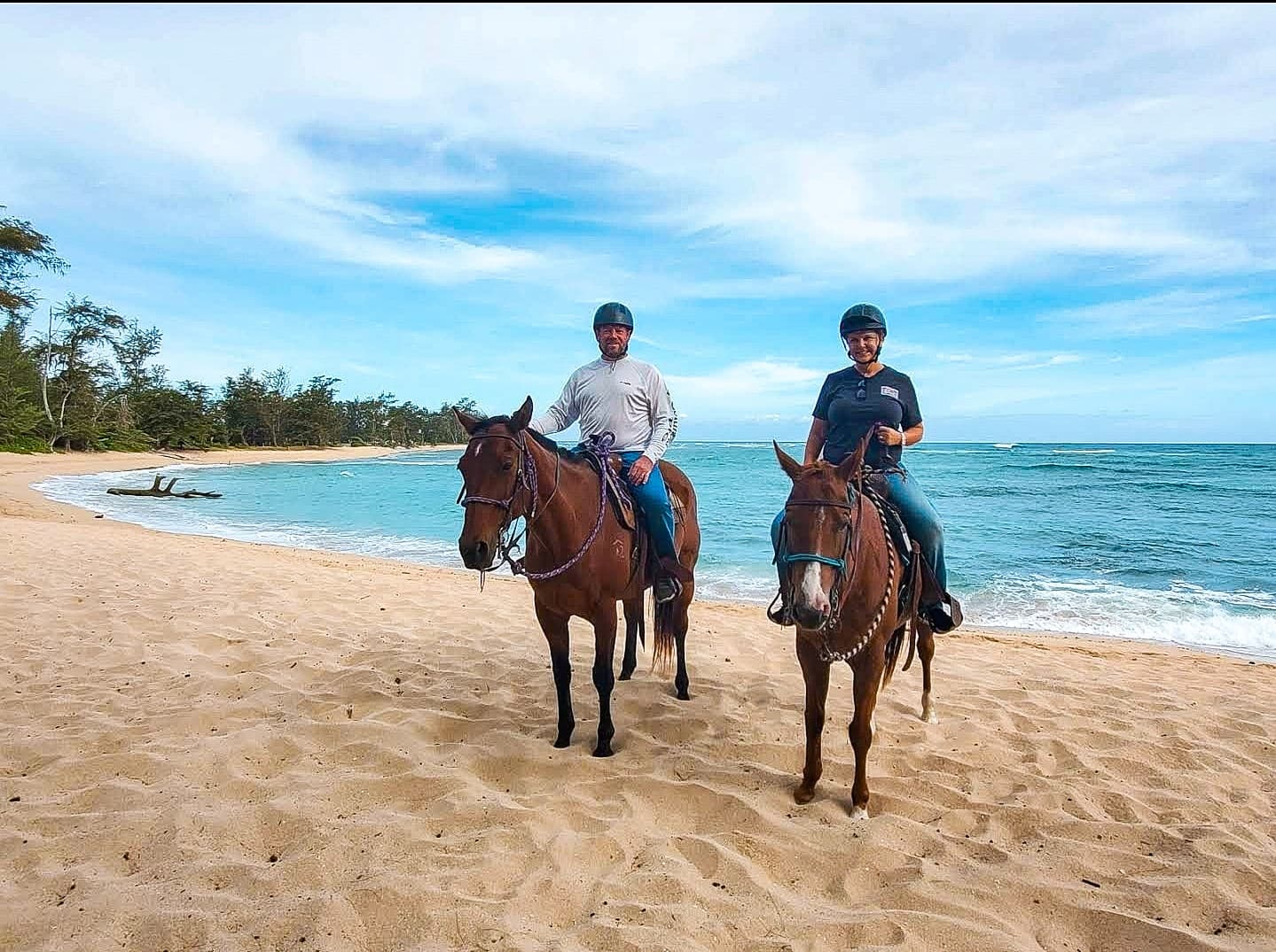 Two riders trotting along a tropical sandy beach shoreline