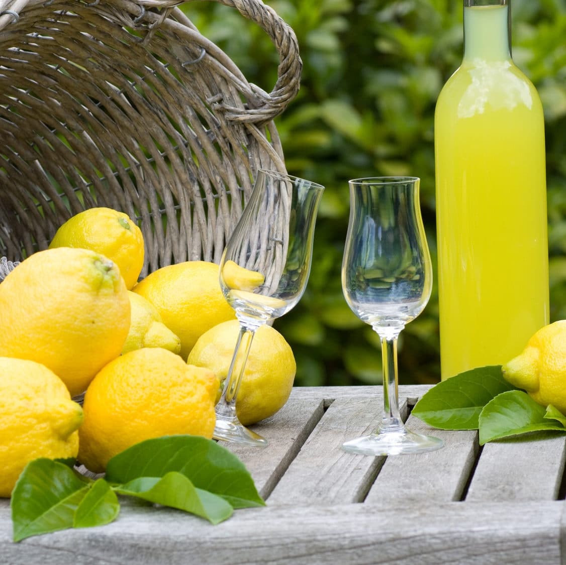 Lemons and limoncello bottle on rustic table in garden