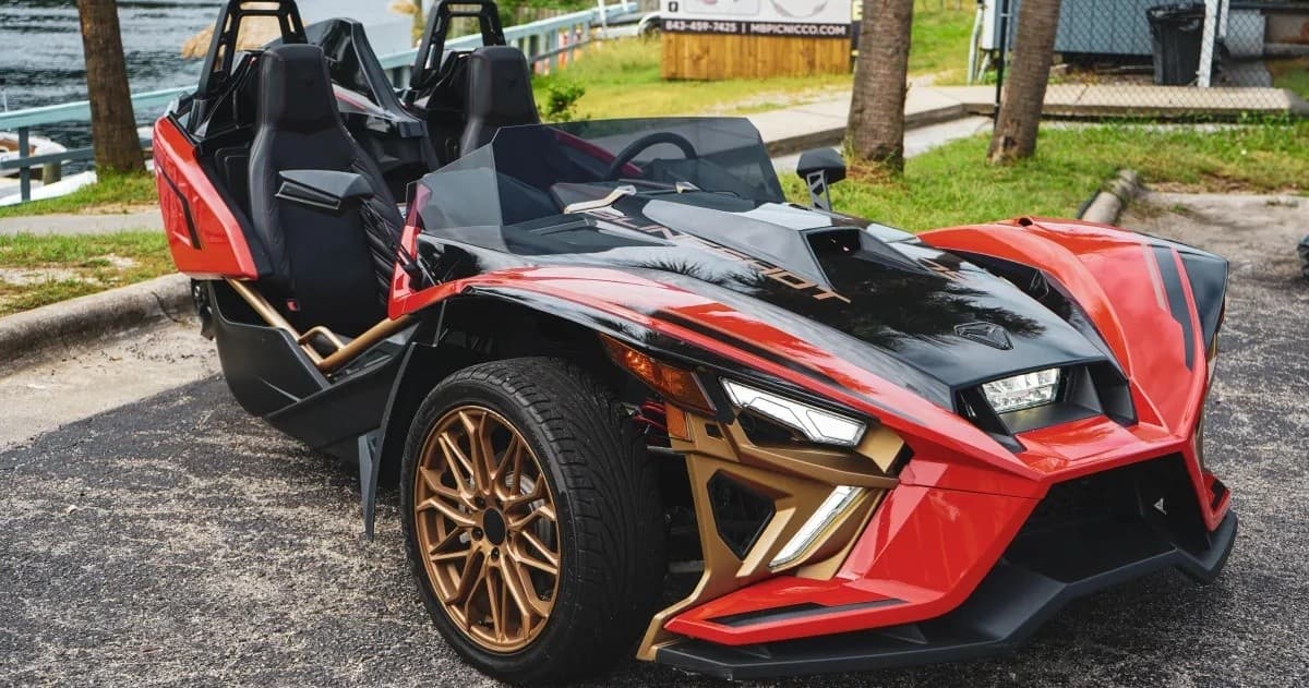 Red three-wheeled slingshot parked near palm trees for scenic drives