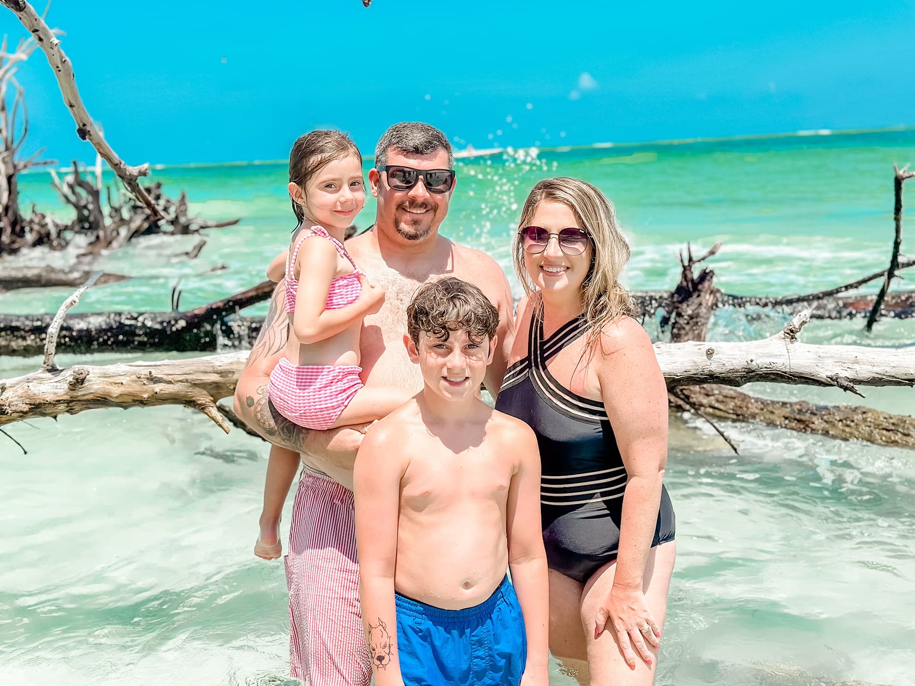 Family posing on sunlit tropical beach with turquoise sea