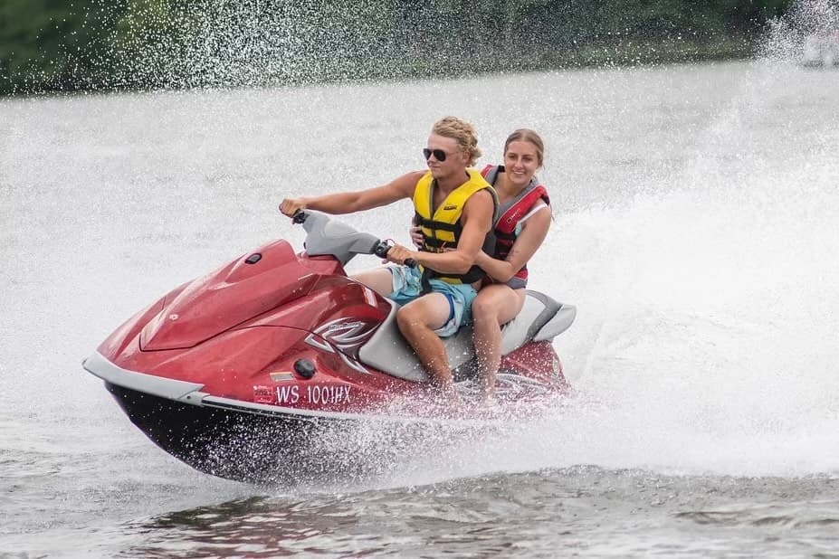 Jet ski riders speeding across lake with dramatic spray