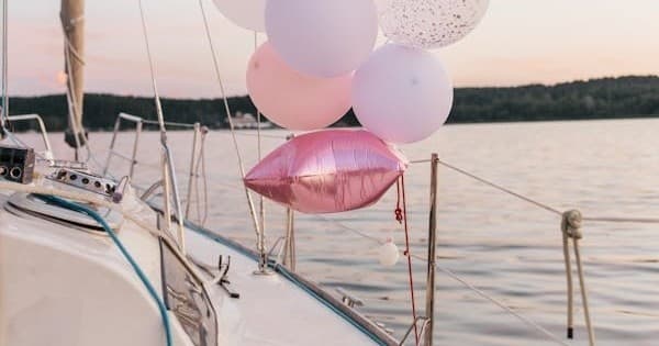 Sailboat deck decorated with pink balloons at calm lakeside sunset