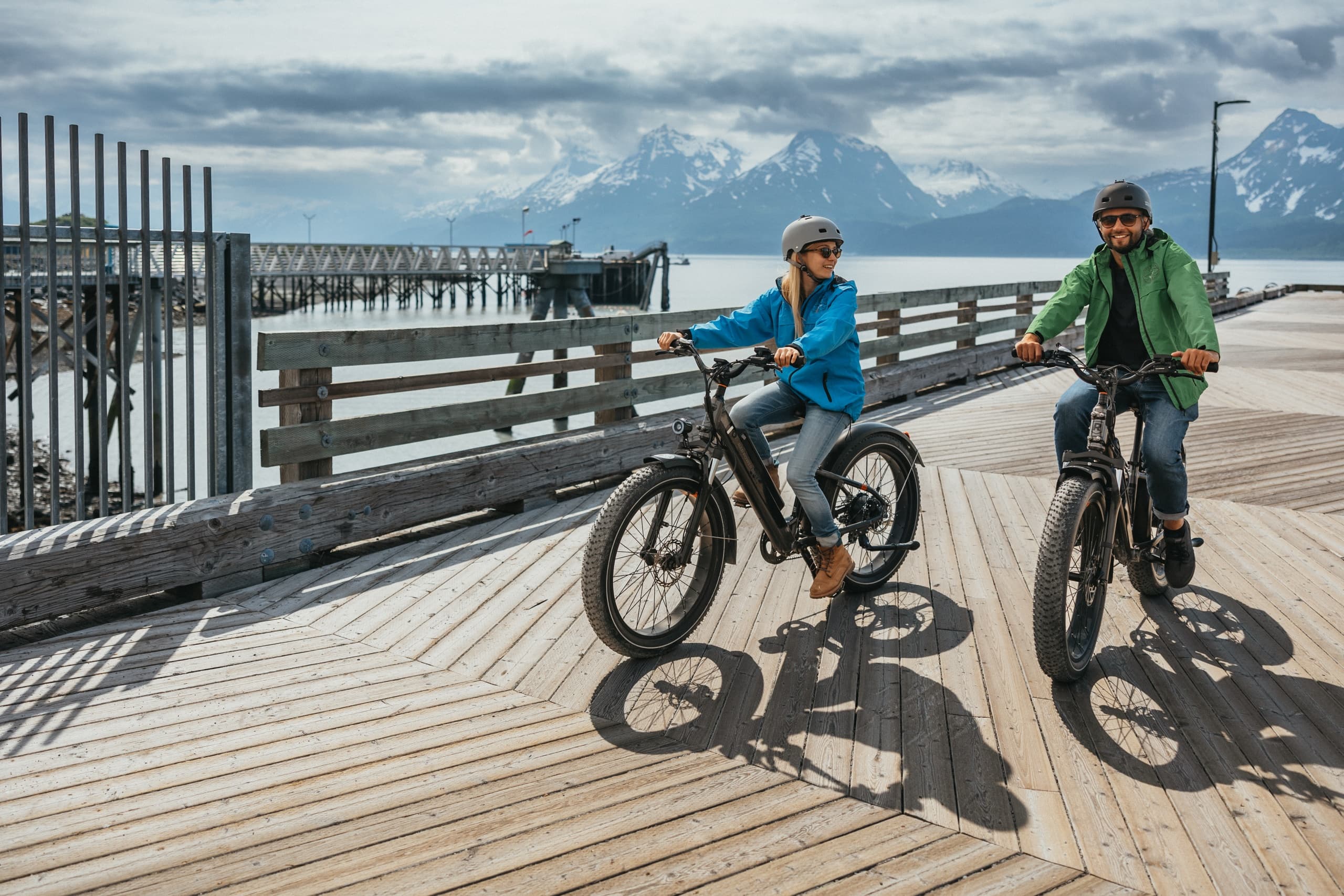 Cyclists riding waterfront boardwalk with mountain views