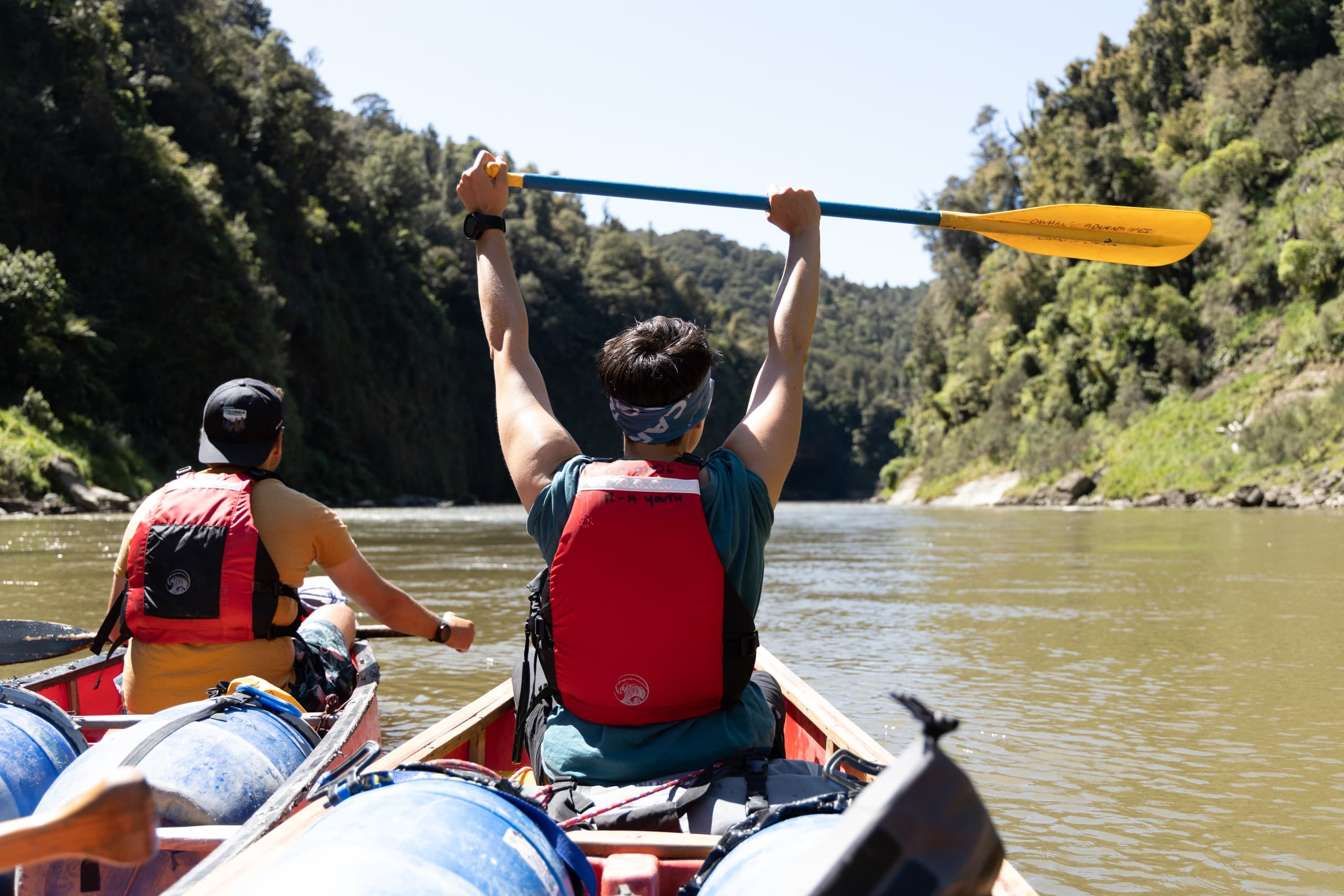 Two paddlers in canoe raising paddle on green river adventure