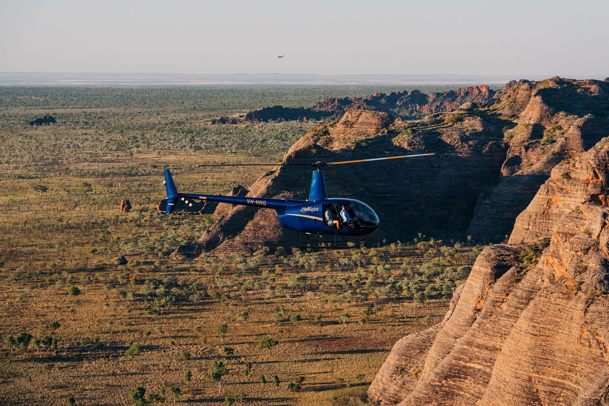 Scenic helicopter skimming escarpment over dry savanna landscape