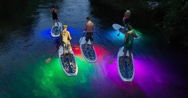 Night glow paddleboarding with illuminated boards on lake