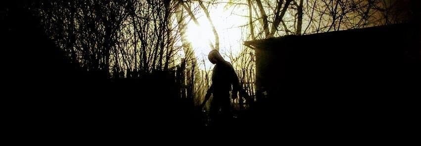 Silhouetted figure walking through eerie wooded yard at sunset