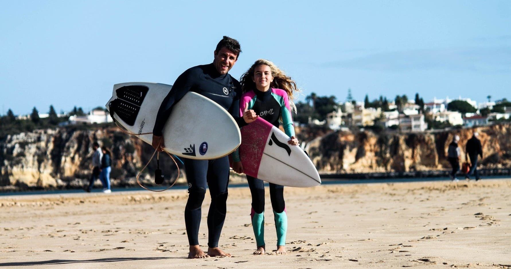Two surfers walking on sandy beach carrying surfboards