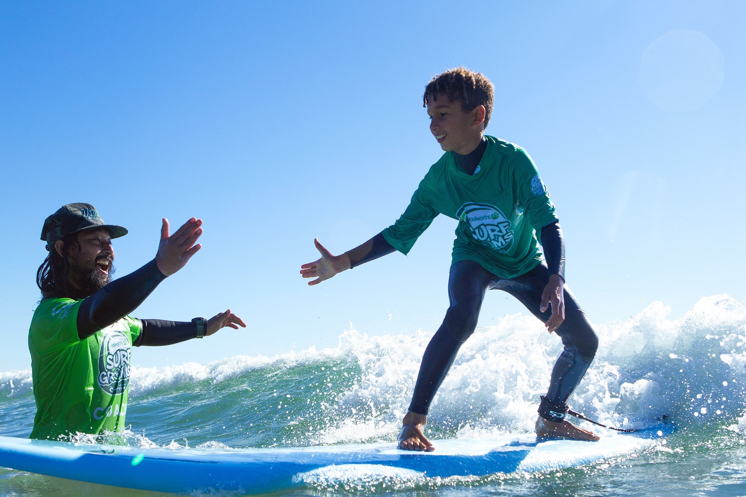 Young surfer high-fiving coach while balancing on a wave