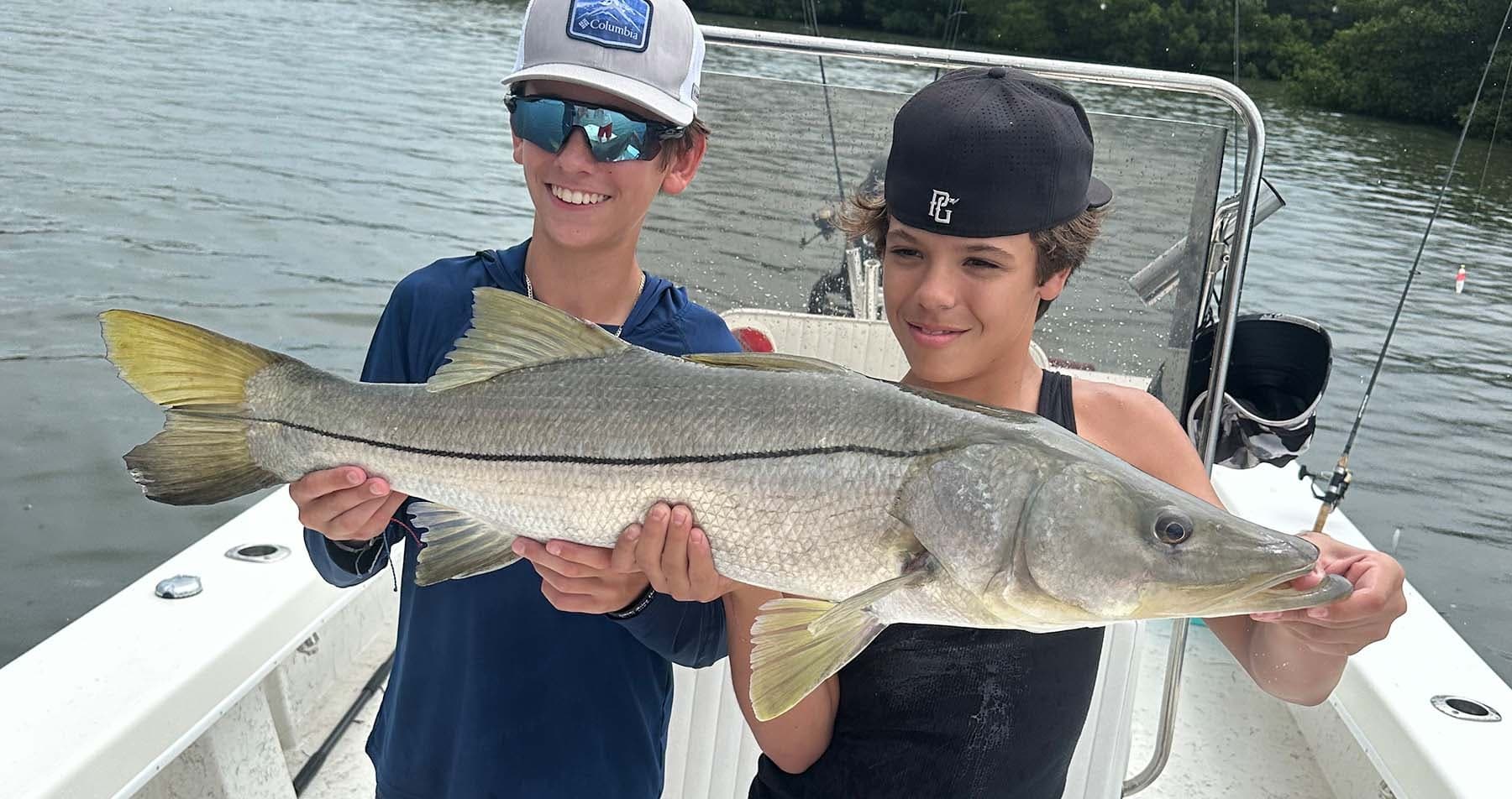 Two kids holding snook aboard boat on coastal waters