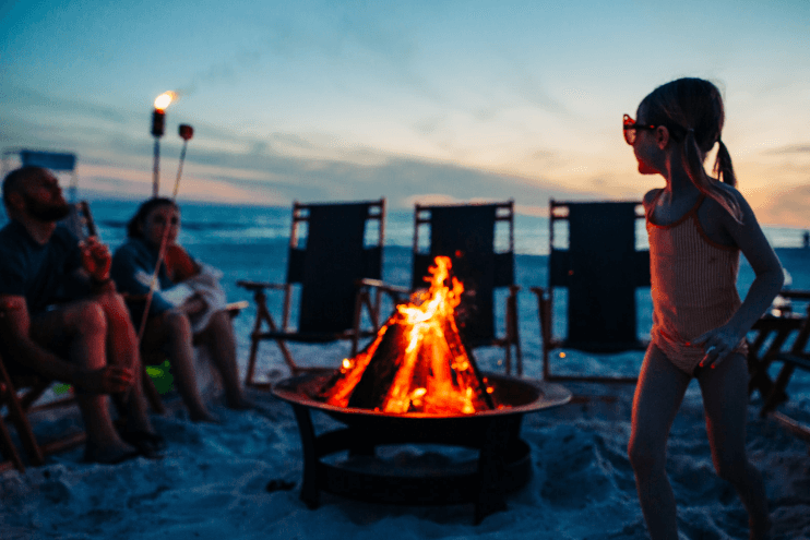 Children and friends by a beach bonfire at dusk on sand