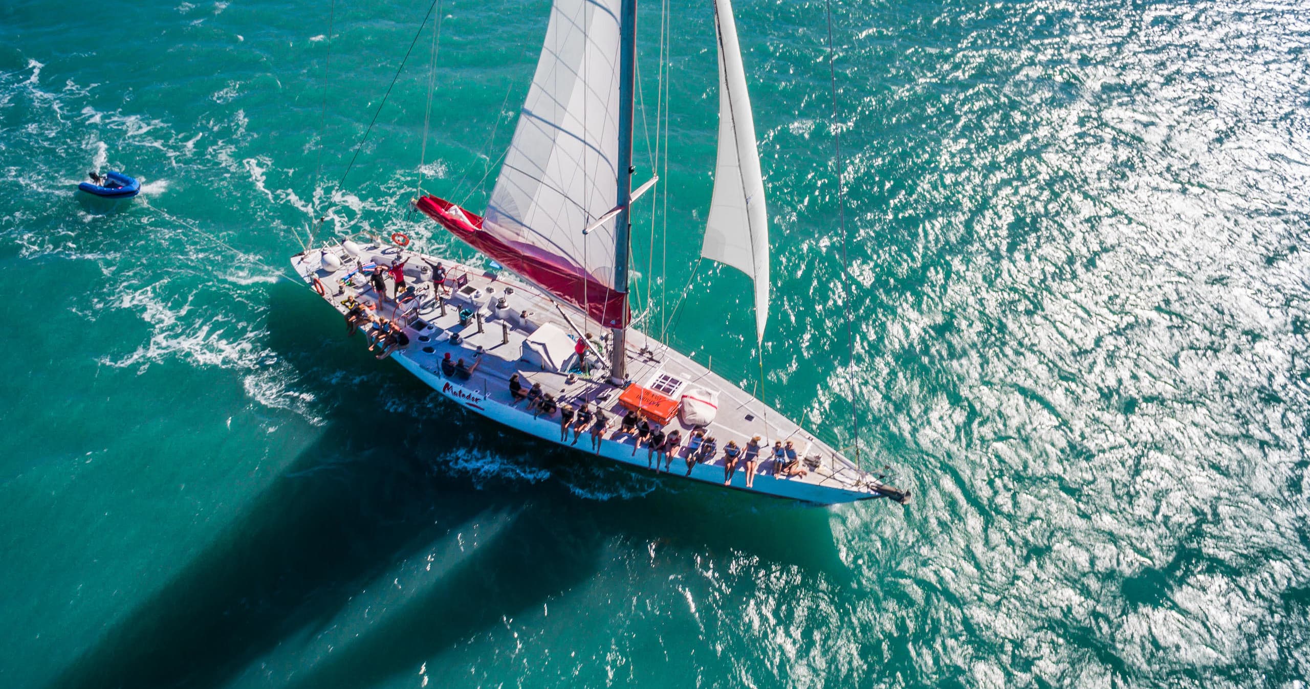 Aerial sailboat cruising vibrant teal sea, high-angle shot
