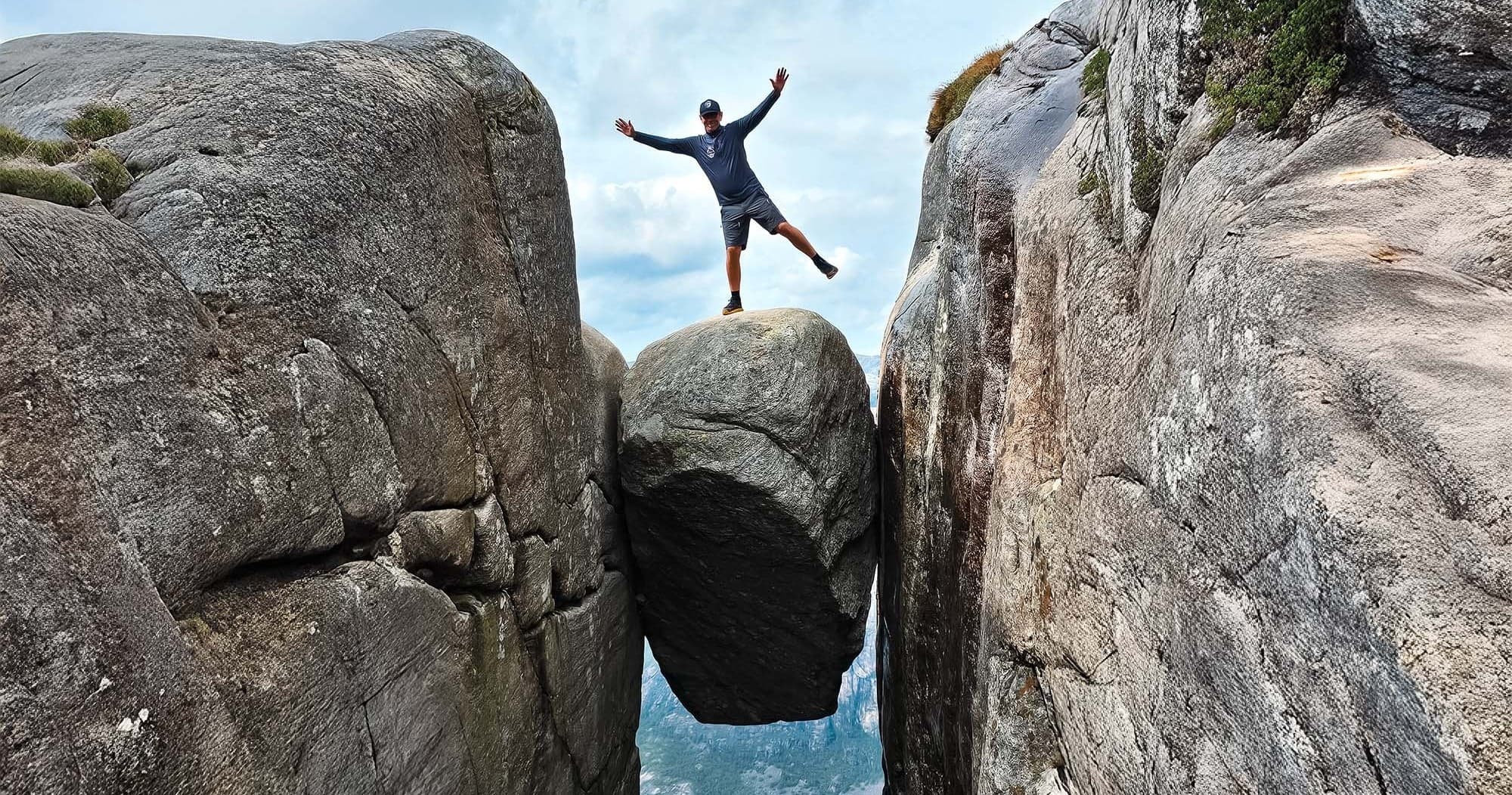 Hiker balancing on Kjeragbolten boulder between cliffs above fjord