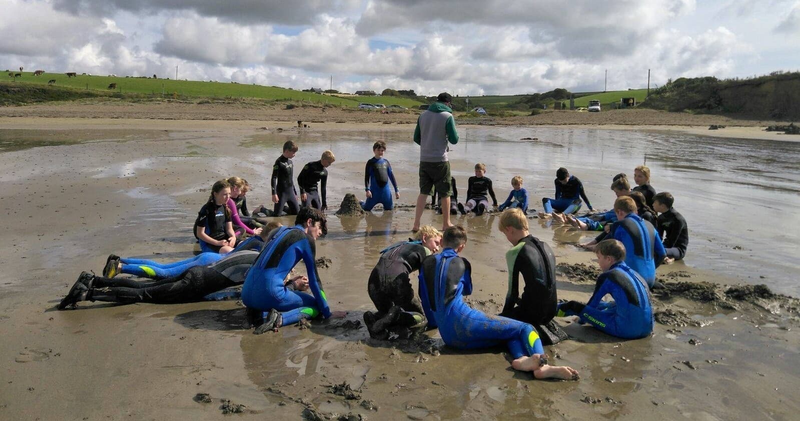 Students in wetsuits practicing beach drills in tidal sand circle