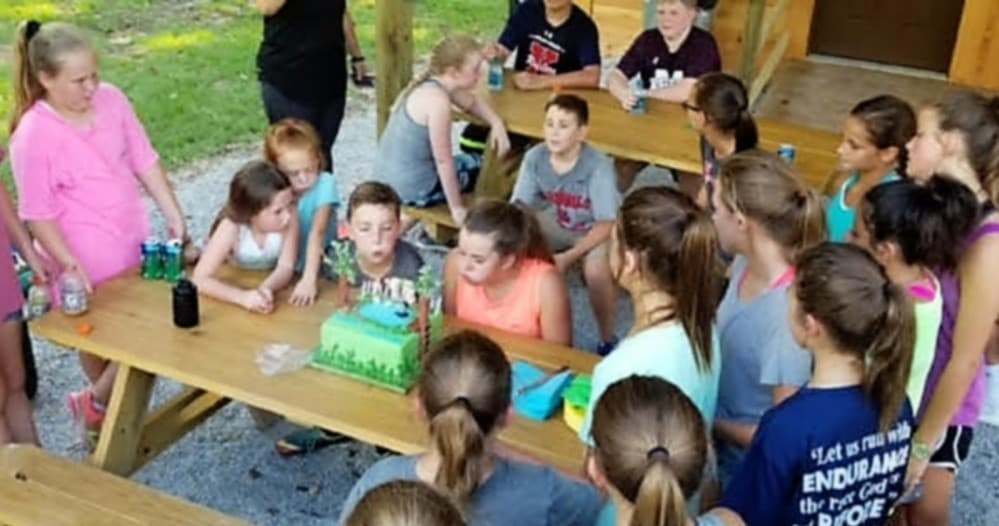 Group of campers gathered at picnic table with cake outdoors