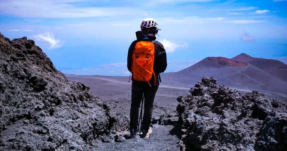 Hiker with orange backpack overlooking Mount Etna volcanic landscape
