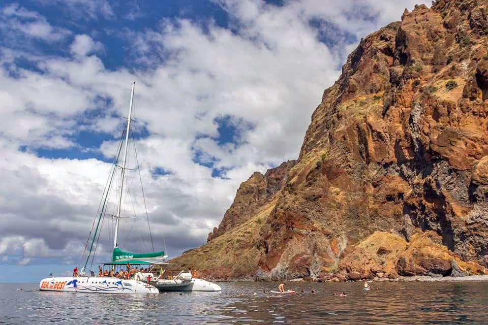 Sailboat cruising past rugged coastal cliffs in clear sea