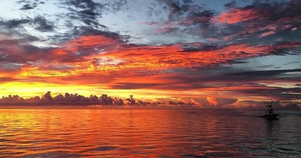 Vibrant ocean sunset over calm sea with silhouetted boat