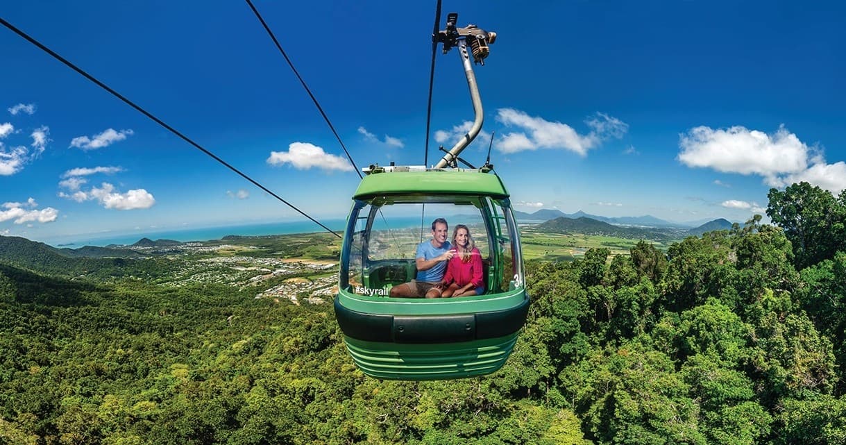Aerial gondola over lush rainforest with mountain skyline view