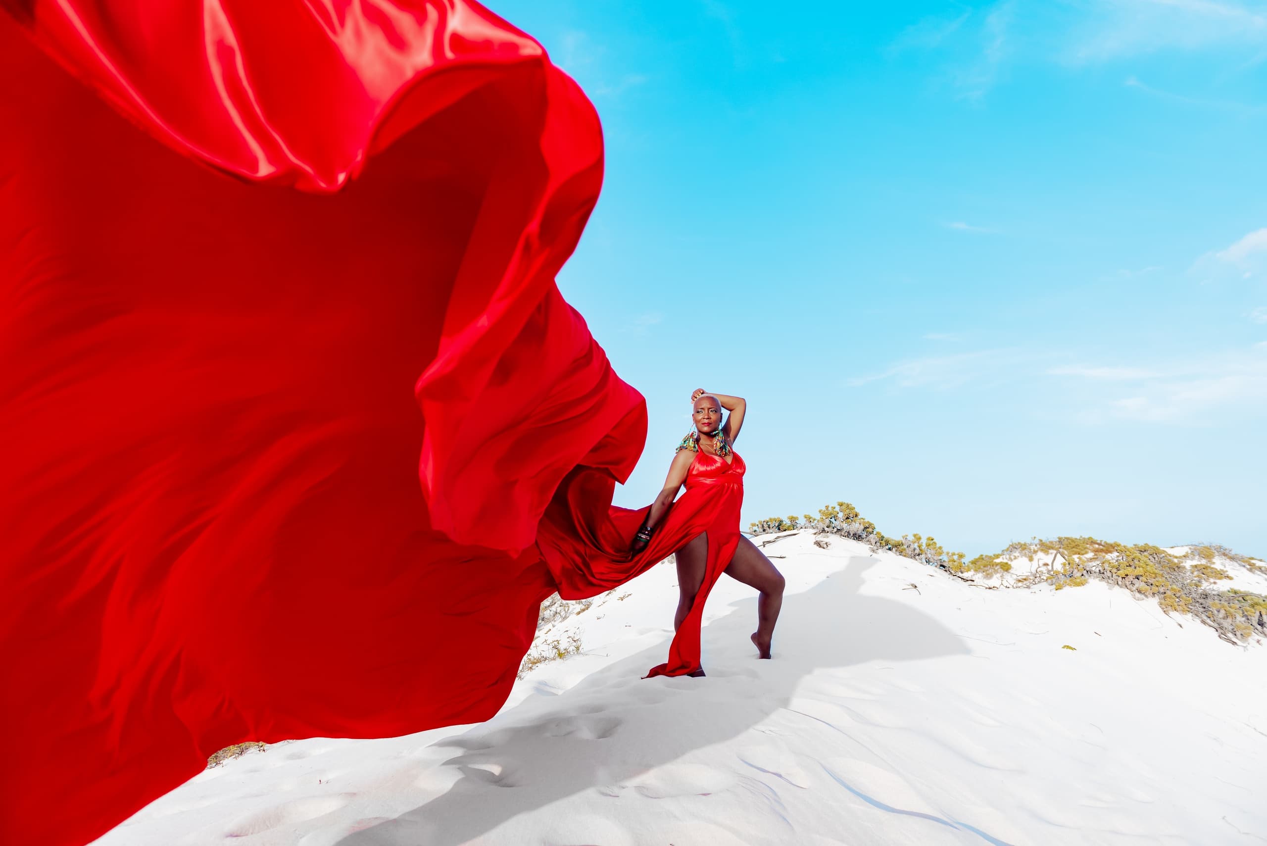 Model posing in red flowing dress on white sand dunes, Aruba beach
